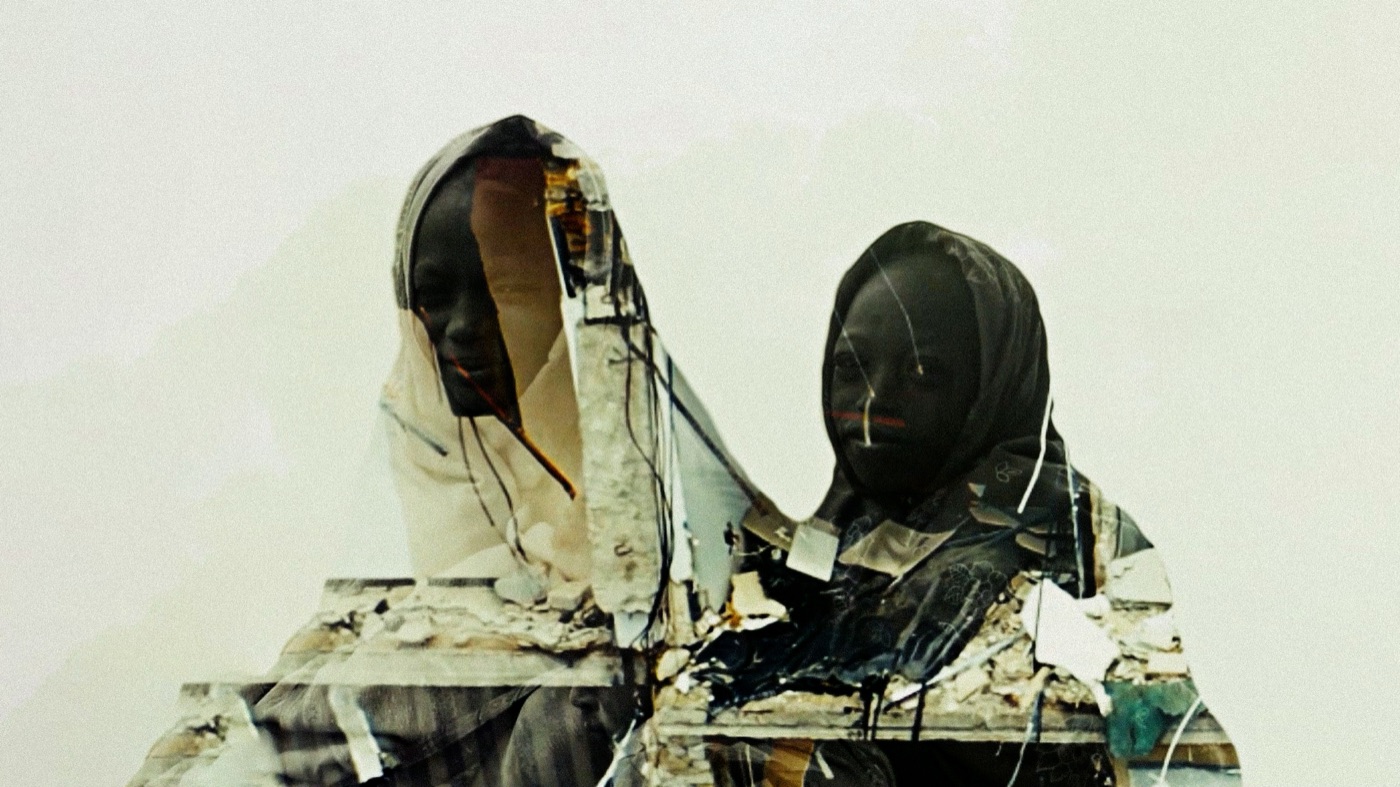 Double exposure of two hooded figures layered with rubble and exposed wiring